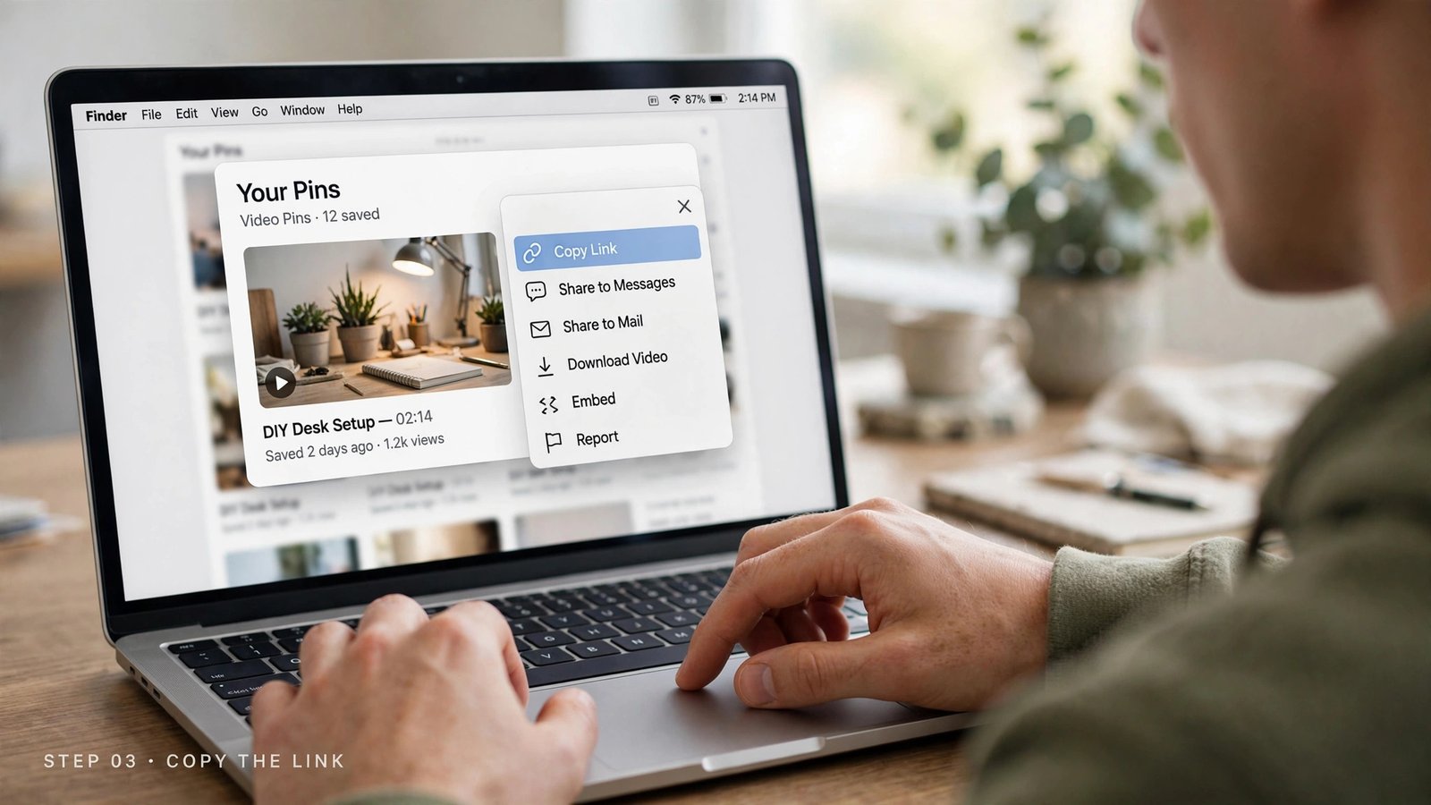 Over-the-shoulder view of hands using a MacBook trackpad while the laptop screen shows a social video pin page with an open share menu and a highlighted Copy Link button, with the macOS menu bar visible.