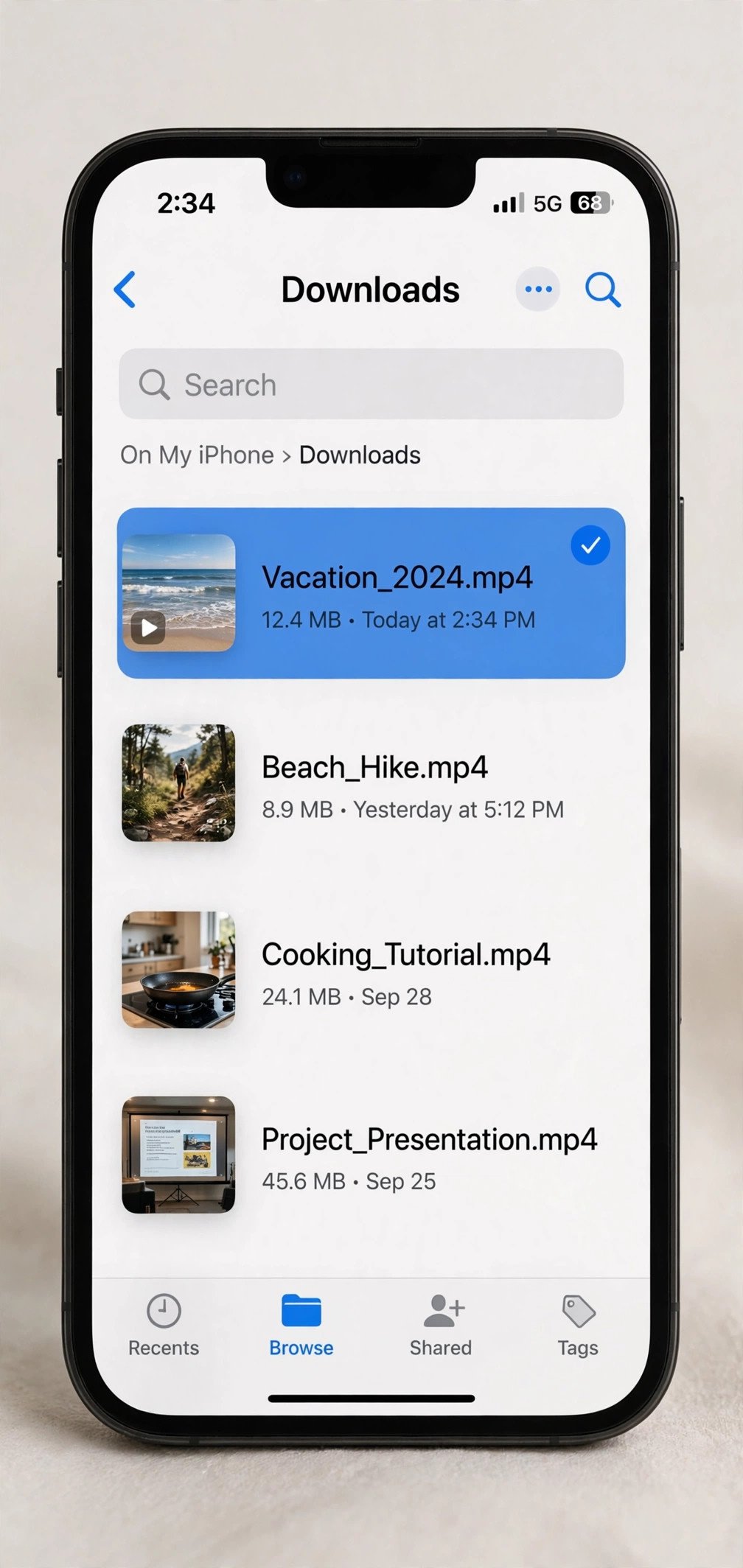 An iPhone showing the iOS Files app open to the Downloads folder, with several MP4 video files listed with thumbnail previews, one file highlighted and selected.